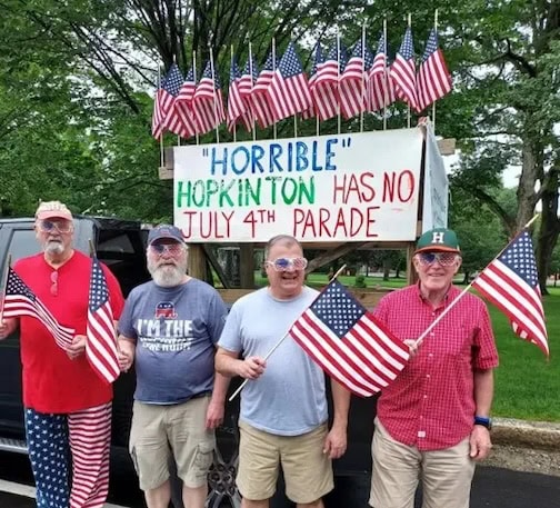 People standing with flags in front of a Horribles Parade sign