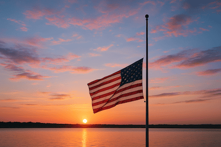 American flag flying half mast at sunset